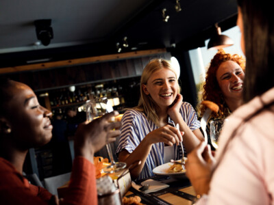 Group of young friends having fun in restaurant, talking and laughing while dining at table.