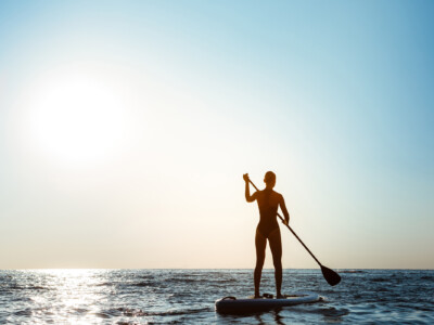 Silhouette of young beautiful girl surfing in sea at sunrise.